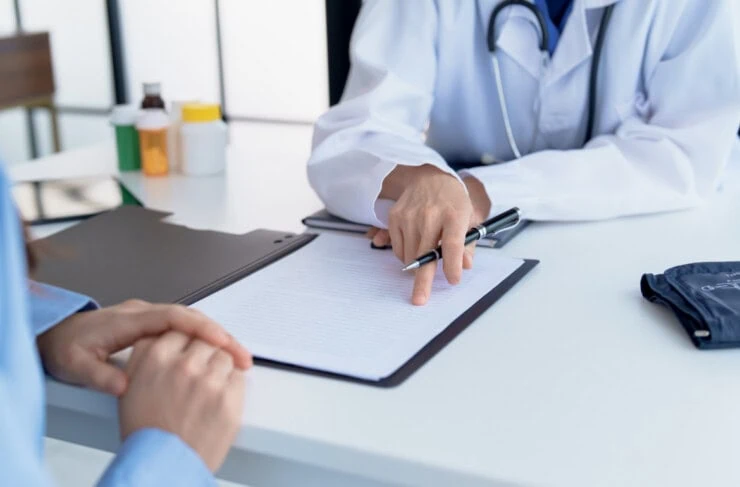 Doctor explaining treatment plan and obtaining informed consent while patient signing consent form in hospital.